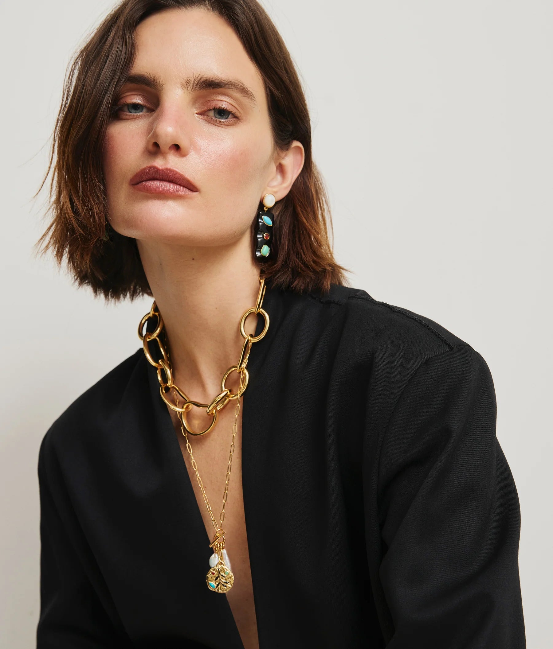 Woman with short brown hair wears a black outfit, the Lizzie Fortunato Campo Charm Necklace, and black and turquoise earrings against a plain light background.