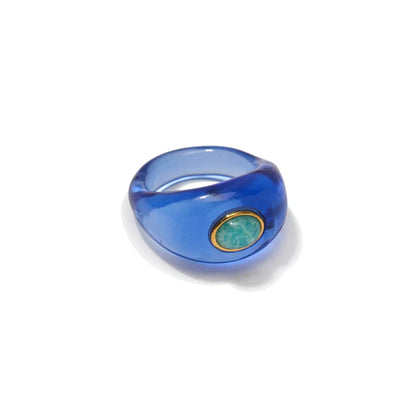The Monument Ring by Lizzie Fortunato is a translucent blue resin band with an oval turquoise stone set in a gold bezel, shown on a white background.