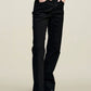 A person stands with hands in pockets against a plain background, wearing a yellow and white striped sleeveless top, the Kallmeyer Farah Classic Bootcut black stretch cotton jeans, and black pointed-toe shoes.