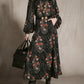 A person wearing a Johanna Ortiz Jacquard Encanto De Isla Ankle Skirt as a high-neck midi dress with a botanical motif, styled with a black belt, gold necklace, black boots, and a black tote bag.