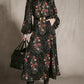 A person wearing a floor-length black Jacquard Intricate Islands Top with a botanical motif, a black belt with an ornate gold buckle, and black boots, holding a black leather tote bag.