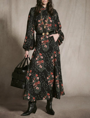 A person wearing a floor-length black Jacquard Intricate Islands Top with a botanical motif, a black belt with an ornate gold buckle, and black boots, holding a black leather tote bag.