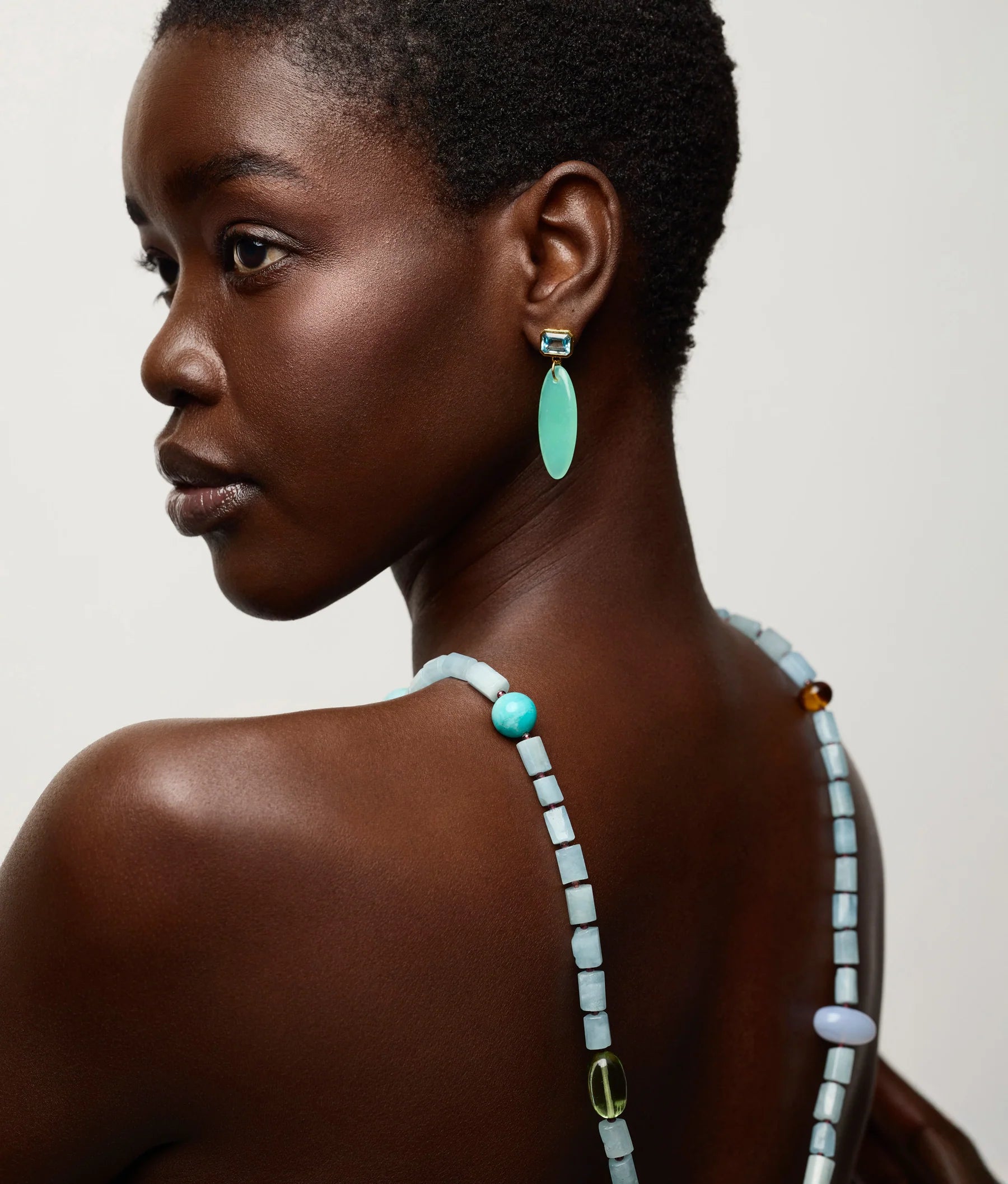 A woman with short hair wears a beaded necklace and the striking Valery Earrings by Lizzie Fortunato, looking over her shoulder against a plain background.