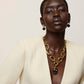 A person with short hair wears a cream blazer, a chunky gold necklace with a dark pendant, and striking Lizzie Fortunato Umbria Earrings that perfectly complement the look.