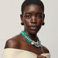 Woman wearing a cream off-shoulder top, Lizzie Fortunato Provence Necklace, and gold earrings, looking at the camera against a neutral background reminiscent of Calder Gardens.