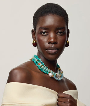 Woman wearing a cream off-shoulder top, Lizzie Fortunato Provence Necklace, and gold earrings, looking at the camera against a neutral background reminiscent of Calder Gardens.