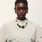 A person wearing a light-colored button-up shirt, the Lizzie Fortunato Acrobat Necklace, and hoop earrings, posing against a plain background.