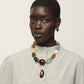 A woman with short hair wears a cream button-up shirt, gold hoop earrings, and the Lizzie Fortunato La Paz Pendant Necklace—a chunky, multicolored bead necklace featuring an amazonite ceramic pendant—set against a neutral background.