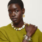 Woman wearing a green sweater, the Lizzie Fortunato Monument Collar necklace, a clear bracelet, and gold earrings poses against a plain white background.