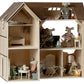 The Maileg Mouse Hole Farmhouse, created by Maileg, is a multi-level wooden dollhouse complete with mouse-size furniture and several small toy mice engaged in various activities across different rooms.