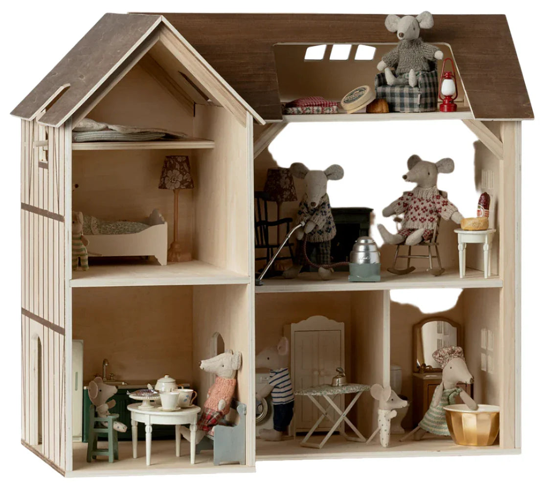 The Maileg Mouse Hole Farmhouse, created by Maileg, is a multi-level wooden dollhouse complete with mouse-size furniture and several small toy mice engaged in various activities across different rooms.