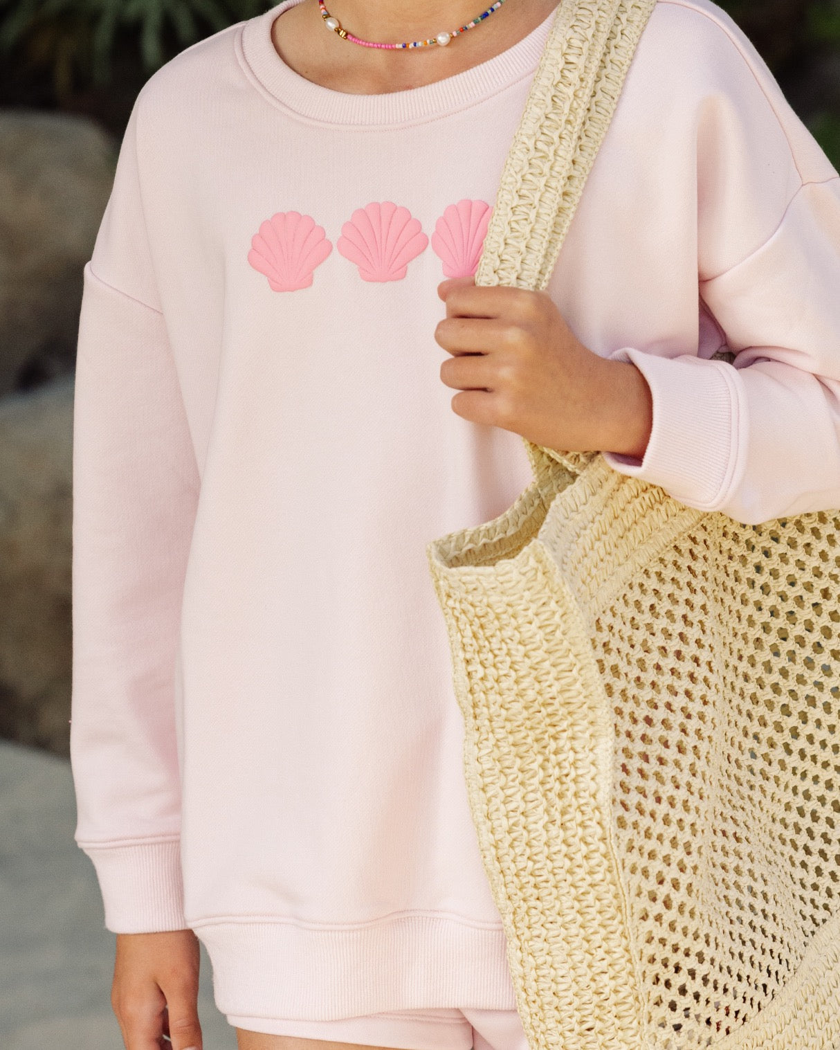 A person wearing the Feather 4 Arrow Baby Girls’ and Girls’ Weekend Sweatshirt in light pink, featuring three pink shell designs in a trendy puff print, holds a large woven tote bag.