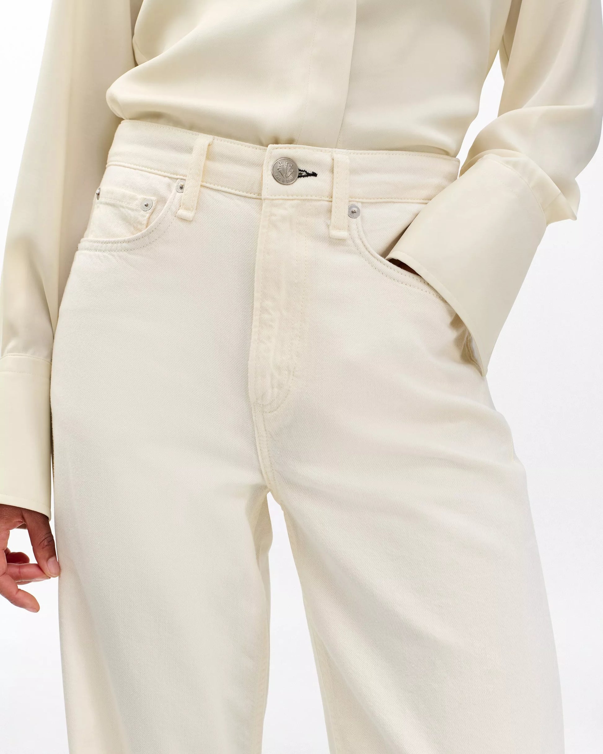 A person wearing Rag & Bone’s Featherweight Logan cream-colored button-up shirt and matching wide leg jeans, with one hand in their pocket.