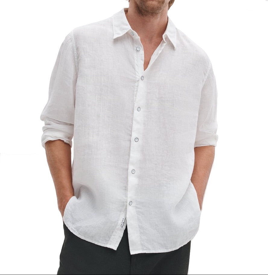 A person wears the Finch Linen Shirt by Rag & Bone—a relaxed fit, long-sleeve white shirt with rolled-up sleeves and hands in pockets—set against a plain white background.