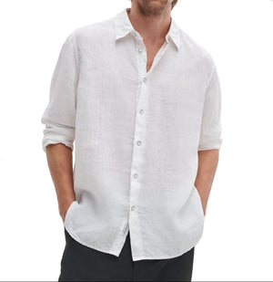 A person wears the Finch Linen Shirt by Rag & Bone—a relaxed fit, long-sleeve white shirt with rolled-up sleeves and hands in pockets—set against a plain white background.