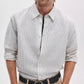 A man facing forward wears the Rag & Bone Finch Linen Stripe Shirt—a light-colored, relaxed-fit button-up featuring thin vertical stripes—paired with tan pants and rolled-up sleeves.
