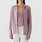 A woman wears the Fine Stripe Showtime Shirt by Guest in Residence—a relaxed fit pink, blue, and white stripe button-down—over a matching top with white pants and layered shell necklaces, posed against a plain background.