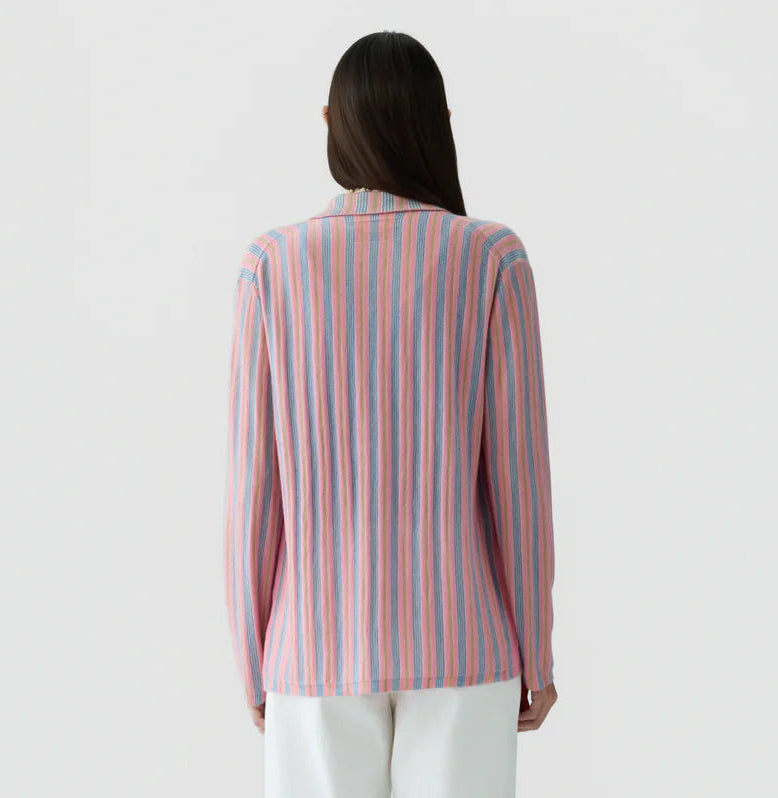 A person with long brown hair is seen from behind wearing the Guest in Residence Fine Stripe Showtime Shirt, featuring relaxed fit stripes in pink, blue, and purple tones, paired with white pants against a plain background.