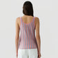 A person with long dark hair is seen from the back against a plain light background, wearing the Fine Stripe Tank by Guest in Residence paired with white pants.
