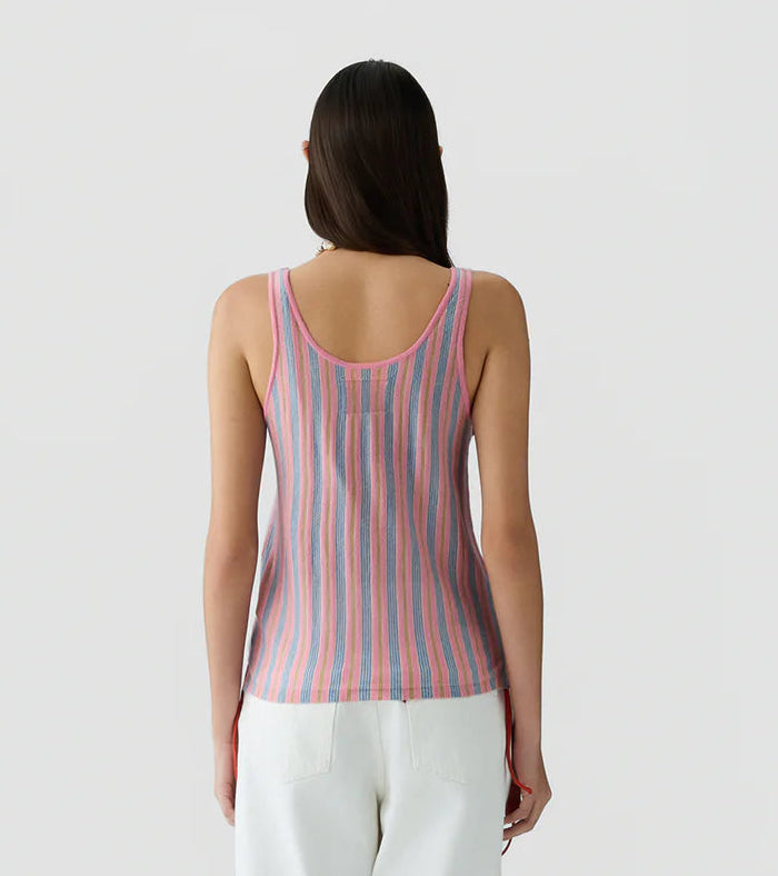 A person with long dark hair is seen from the back against a plain light background, wearing the Fine Stripe Tank by Guest in Residence paired with white pants.