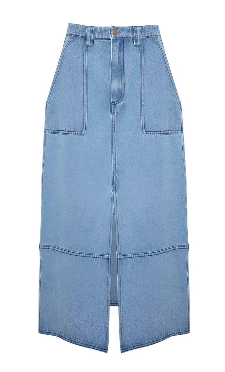 The Parke Skirt by Hunter Bell NYC is a light blue midi denim skirt with a stylish front seam and slit, featuring two large front pockets and a waistband with button closure.