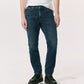 A person wearing a white T-shirt, Rag & Bone Fit 2 Authentic Stretch Denim jeans in dark indigo, and black shoes stands against a plain light background.