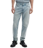 A person wearing Rag & Bone Fit 3 Authentic Stretch light blue tapered leg jeans and black shoes, standing with arms relaxed at their sides, shown from shoulders to feet.