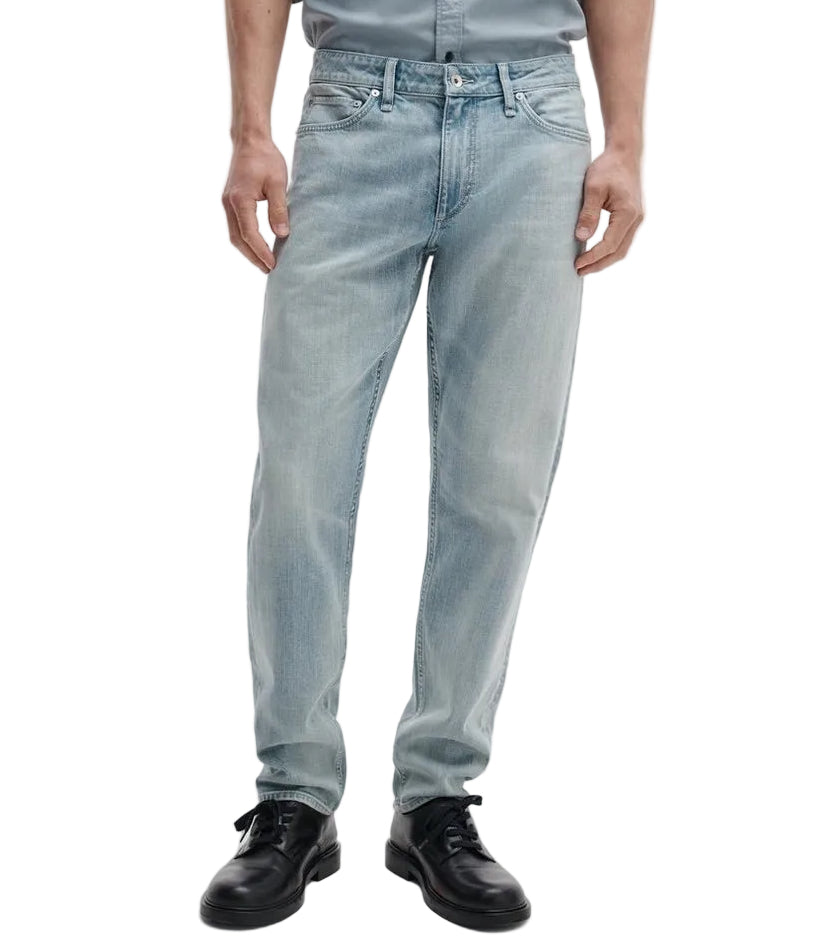 A person wearing Rag & Bone Fit 3 Authentic Stretch light blue tapered leg jeans and black shoes, standing with arms relaxed at their sides, shown from shoulders to feet.