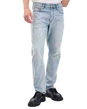Someone wearing Rag & Bone Fit 3 Authentic Stretch light indigo jeans, a white shirt, and black shoes stands with one hand in their pocket.