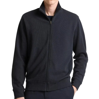 A person wearing the vince Flat Back Piqué Full Zip, a black cotton-blend jacket with a high collar and minimal silhouette, hands in pockets, shown from shoulders to hips.
