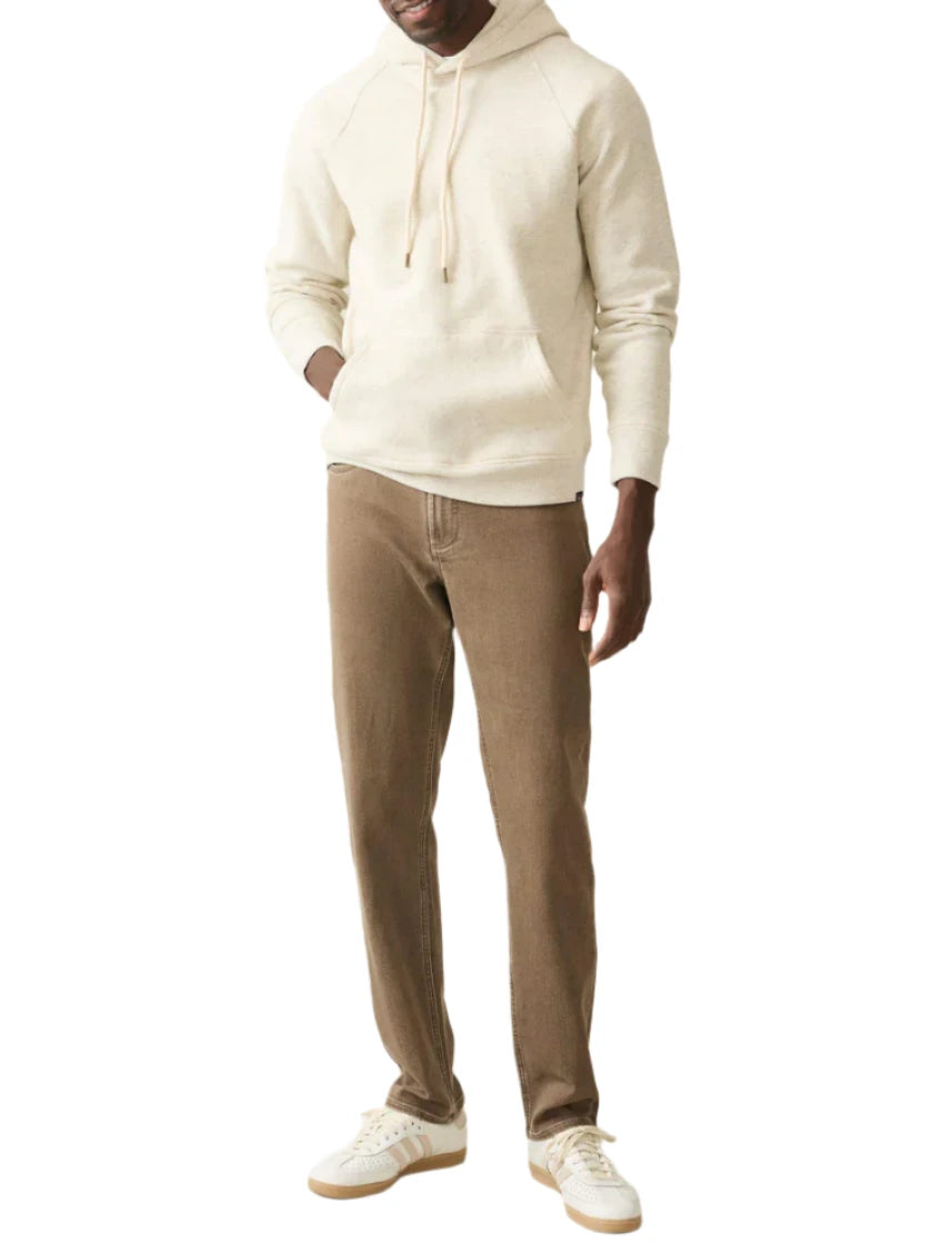 A person in a super soft High Standard Fleece Hoodie from Faherty, featuring a beige color and organic cotton fabric, complemented by brown pants and white sneakers, stands against a plain white background.