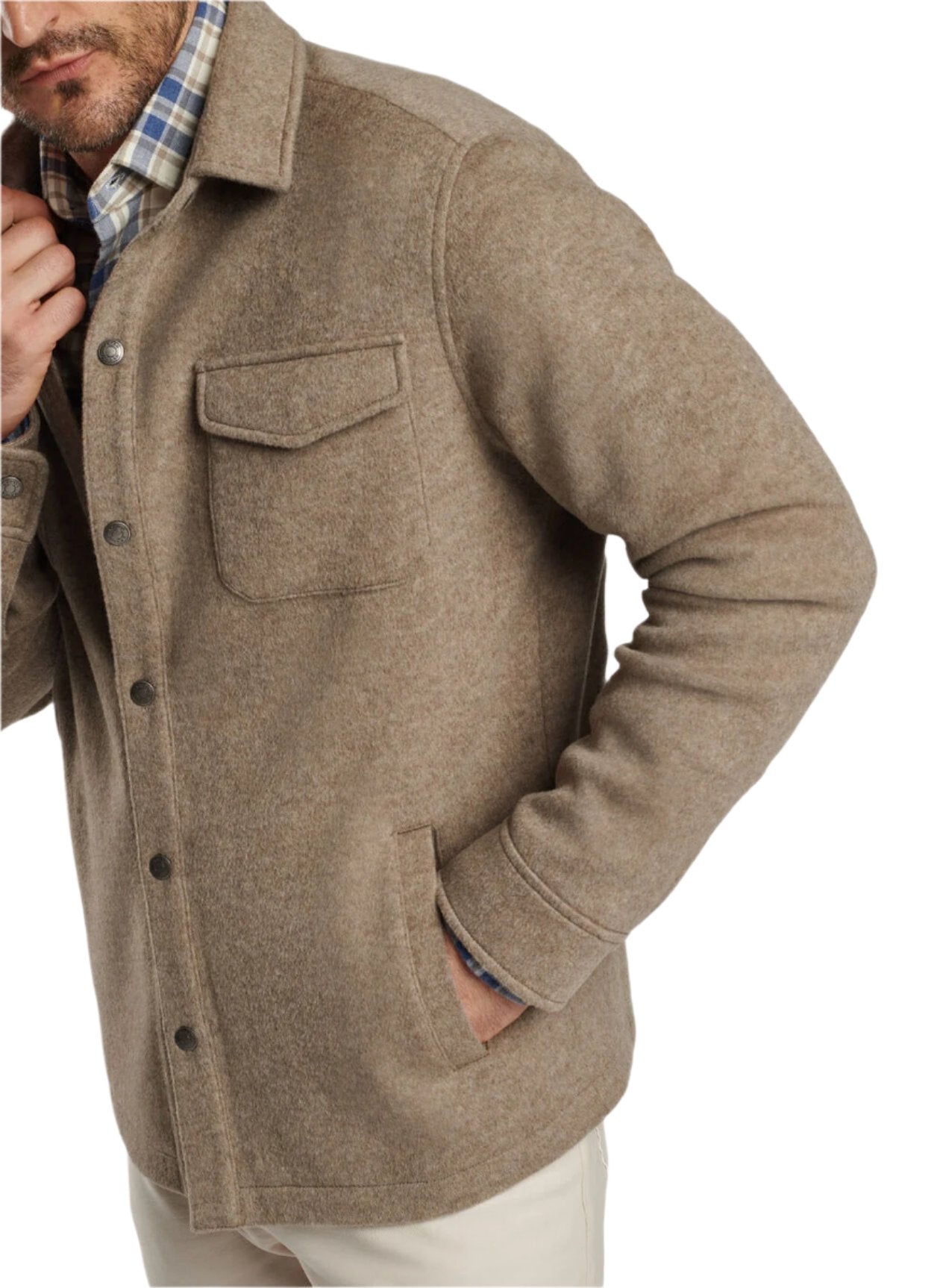 A person wearing the Peter Millar Crown Flex Fleece Shirt Jacket, a men's wool jacket in brown crafted from stretch knit fabric with a single chest pocket and button closures, layered over a plaid shirt and complemented by white pants.