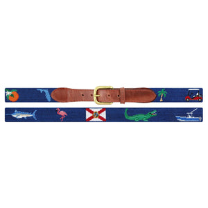 Introducing the Florida Life Belt by Smathers & Branson—a blue needlepoint belt featuring a brown Italian leather buckle and hand-stitched, embroidered images of an orange, the Florida map, a fish, flamingo, state flag, alligator, golfer, golf cart, and boat.