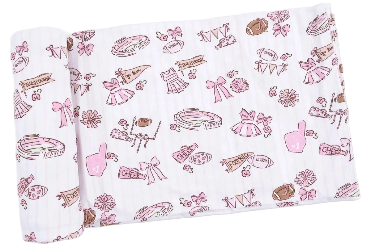 A rolled-up Angel Dear Swaddle Blanket in white, made from Viscose from Bamboo, decorated with pink and brown cheerleading and football-themed illustrations—including pom-poms, megaphones, and uniforms—perfect for your little one.