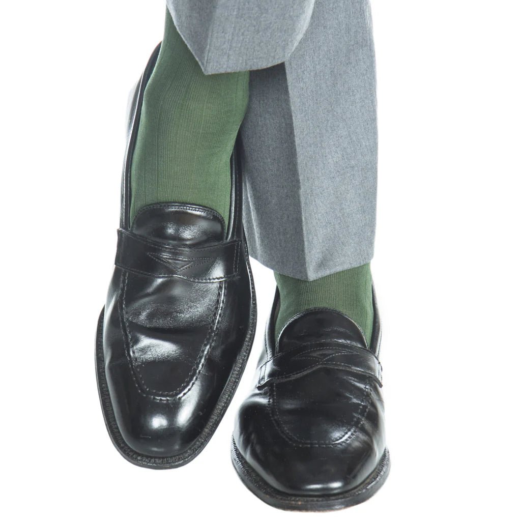 A person wearing gray pants, Dapper Classics Forest Green Ribbed Cotton Sock Linked Toe Mid-Calf, and black leather loafers with legs crossed.