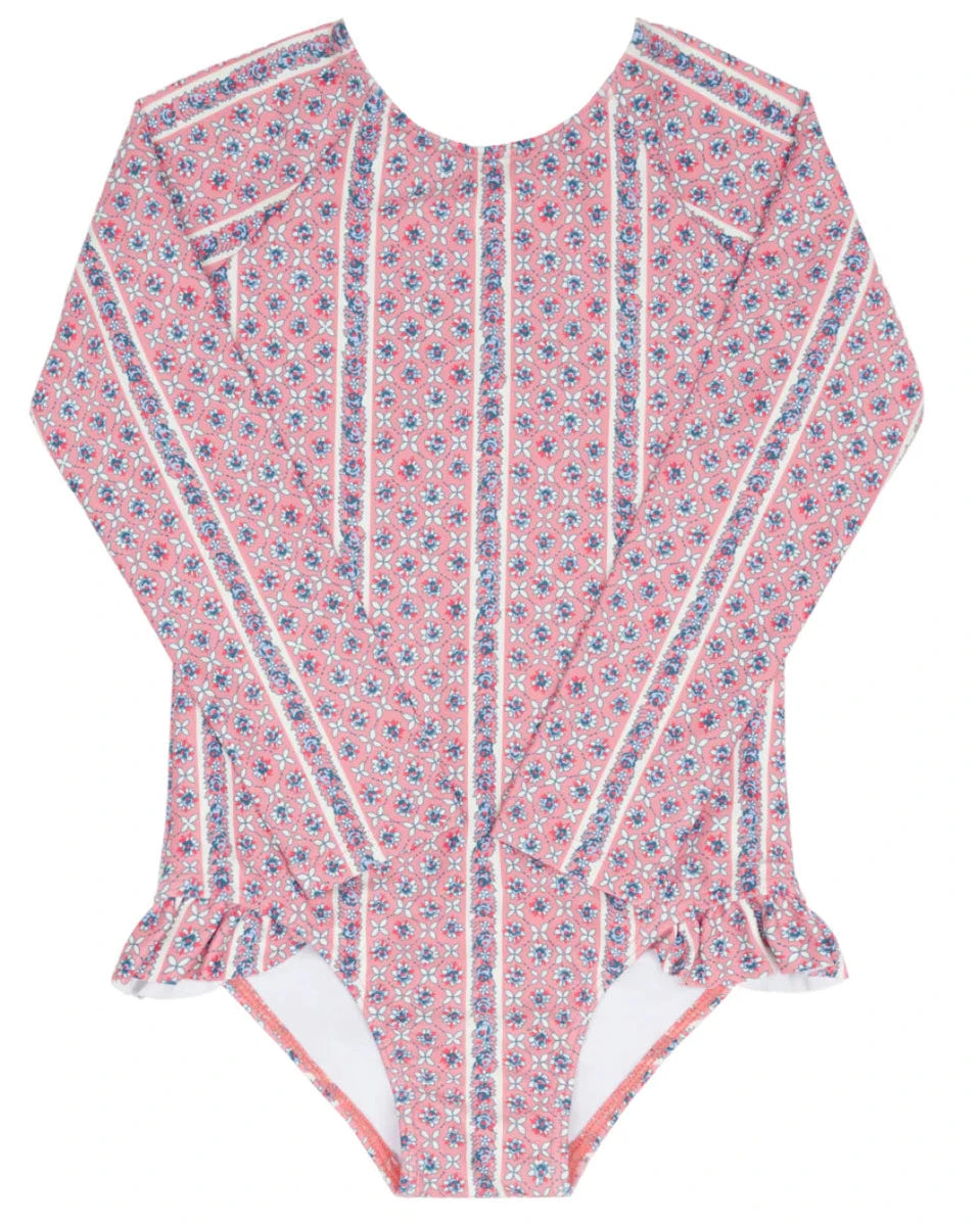 The Minnow Girls' Floral Tile Rashguard One Piece features pink long sleeves, a small floral tile print, vertical white stripes, and hip ruffles for stylish, sun-safe swimwear.