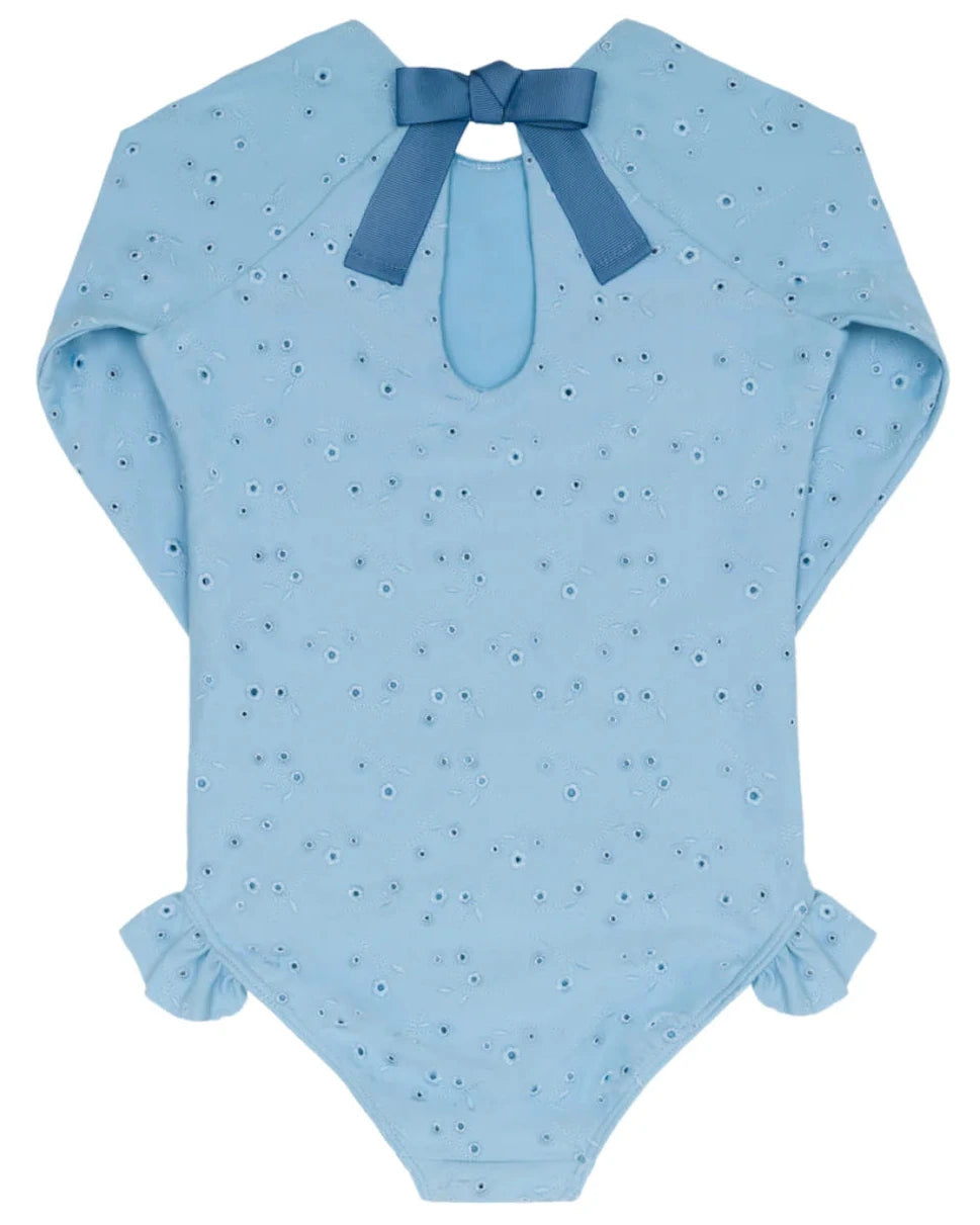 Minnow Girls' Eyelet Rashguard One Piece features light blue eyelet details, a back keyhole opening, ruffled sleeves and legs, hip ruffle accents, and a blue ribbon bow at the neckline.