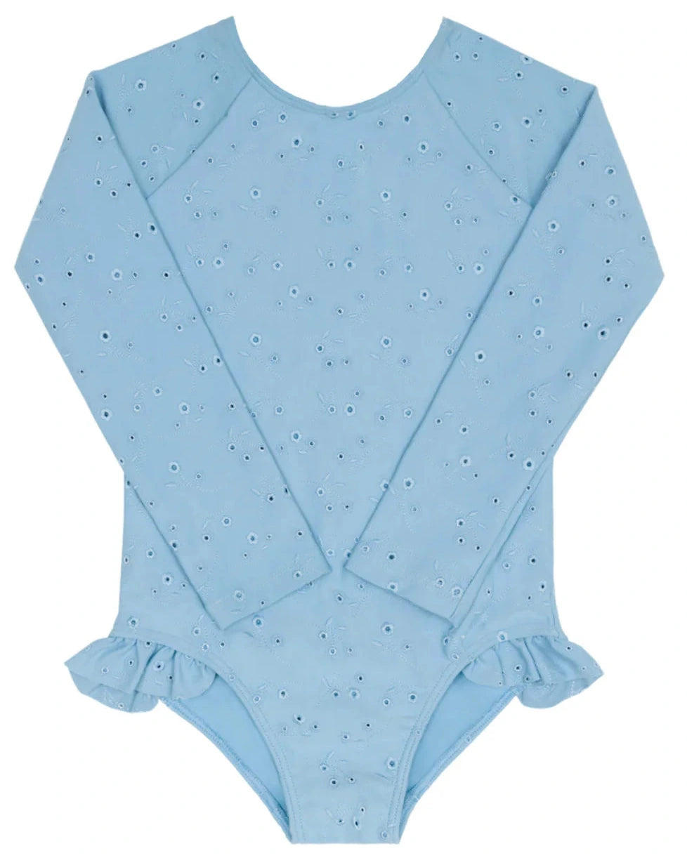 The Minnow Girls’ Eyelet Rashguard One Piece is a light blue, long-sleeve swimsuit featuring an eyelet pattern and ruffle hip detail, shown flat on a white background.