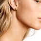 Close-up profile view of a person wearing a simple gold pair of Luna Earrings from Lie Studio on their left ear, with shoulder-length blonde hair and fair skin.