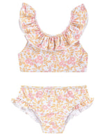 The Girls' Primavera Bikini Set by Louise Misha features a charming floral pattern with ruffled sleeves on the top and a ruffled waist on the bottoms. This two-piece set comes in delightful colors of pink, yellow, and white.