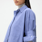 A person with long dark hair wears the TWP Next Ex Stripe Shirt in a boxy silhouette over a light gray turtleneck, standing against a plain white background.