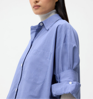 A person with long dark hair wears the TWP Next Ex Stripe Shirt in a boxy silhouette over a light gray turtleneck, standing against a plain white background.