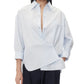 A person stands against a plain white background, looking directly at the camera, wearing the TWP New Earl Shirt—a relaxed, oversized, light blue button-down—paired with dark pants.