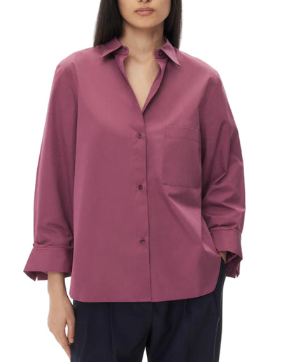 A person wearing the TWP Next Morning Shirt—an oversized mauve button-down with long sleeves, a left chest pocket, and a relaxed silhouette—paired with dark trousers.