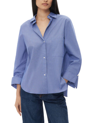 A woman wears the TWP Next Morning Top, a relaxed light blue cotton poplin shirt with long sleeves, chest pocket, and open collar, paired with dark blue jeans.
