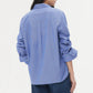 A person is shown from the back against a plain background, wearing the TWP Next Morning Top in light blue paired with blue jeans.