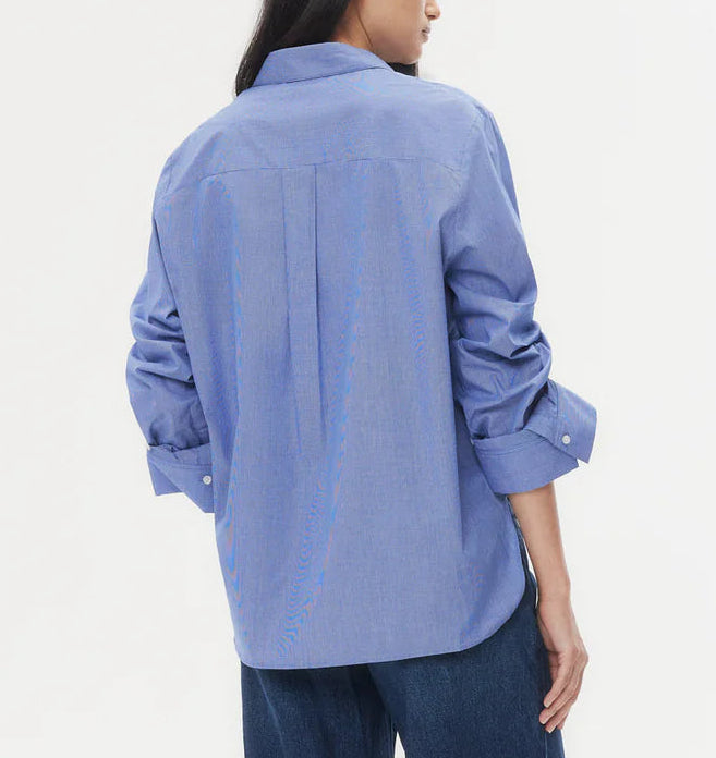 A person is shown from the back against a plain background, wearing the TWP Next Morning Top in light blue paired with blue jeans.
