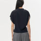 A person with long dark hair stands facing away, wearing the TWP Wish You Would Top and gray wide-leg pants against a plain white background.