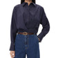 A woman wearing the TWP Taken Shirt, a relaxed navy button-down, tucked into high-waisted blue jeans with a brown belt, stands against a white background.