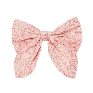 The Louise Misha Gilla Hair Clip is a pink fabric bow with a floral pattern, two wide loops, and angled tails—perfect as a charming floral accessory.